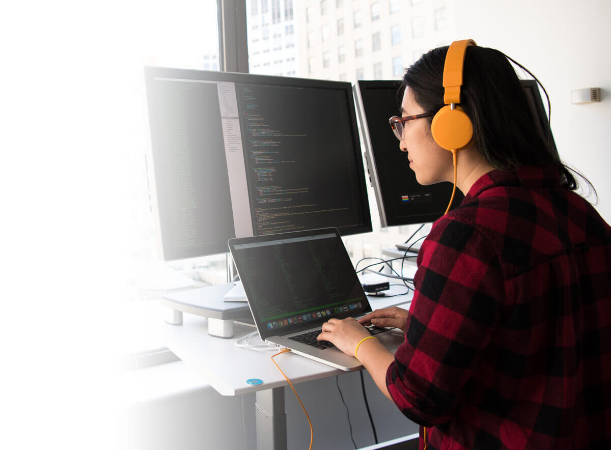 Woman with headphones working on multiple monitors